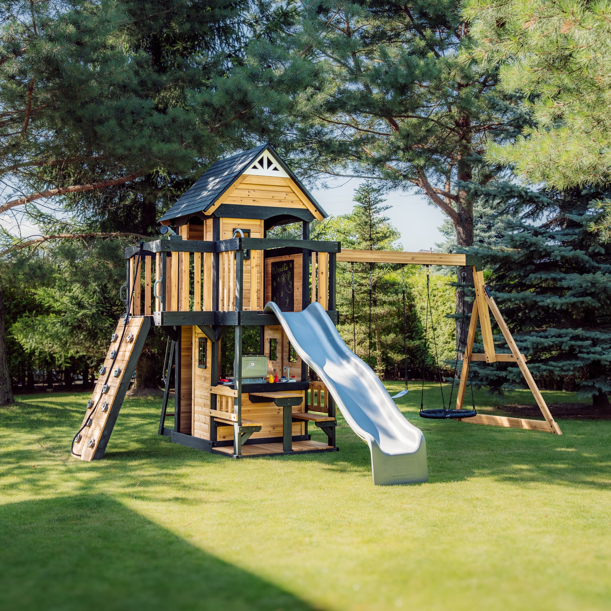 Canyon Creek cedar swing set in a garden with upper fort, grey wave slide, rock climbing ramp and A-frame swing beam